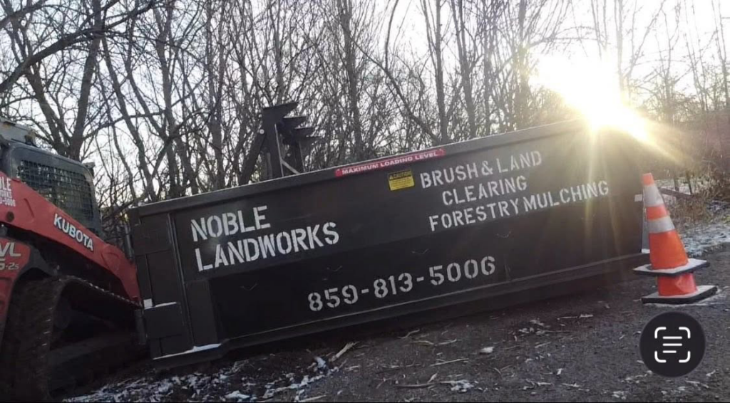 A Kubota skid steer next to a Noble Landworks dumpster for brush and land clearing in Georgetown, KY.