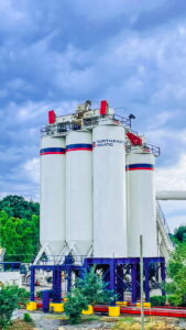 Tall asphalt plant silos with the Northeast-Paving logo clearly visible at their facility in Bangor, ME