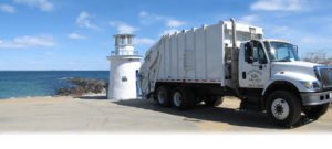 An Oceanside Rubbish Inc junk removal truck parked by a lighthouse and the ocean in Sanford, ME.