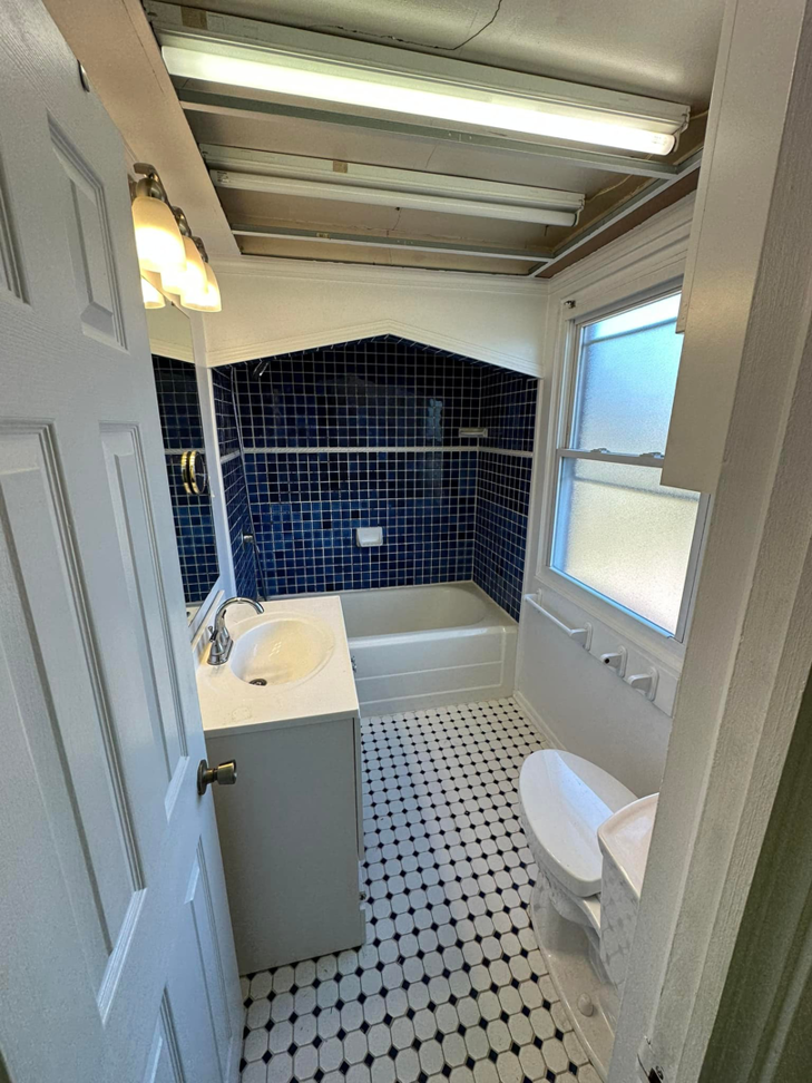 An old bathroom before renovation, showing blue tiles and an exposed ceiling, by Tap & Tile Inc. in East Pittsburgh, PA.