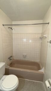 An old, worn brown bathtub and tiled walls before refinishing by Phillys Finest Tub & Tile Refinishing in Philadelphia, PA