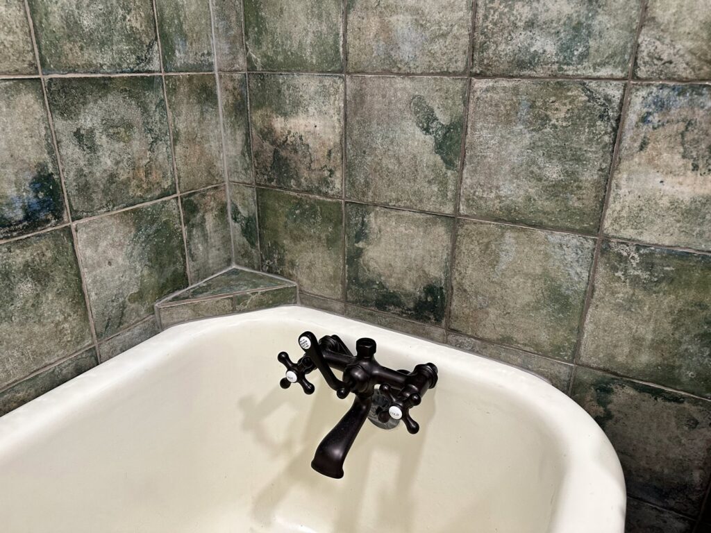 A close-up of an old bathtub faucet and green-toned wall tiles, showing potential for renovation by Tile Jawn in Philadelphia, PA.