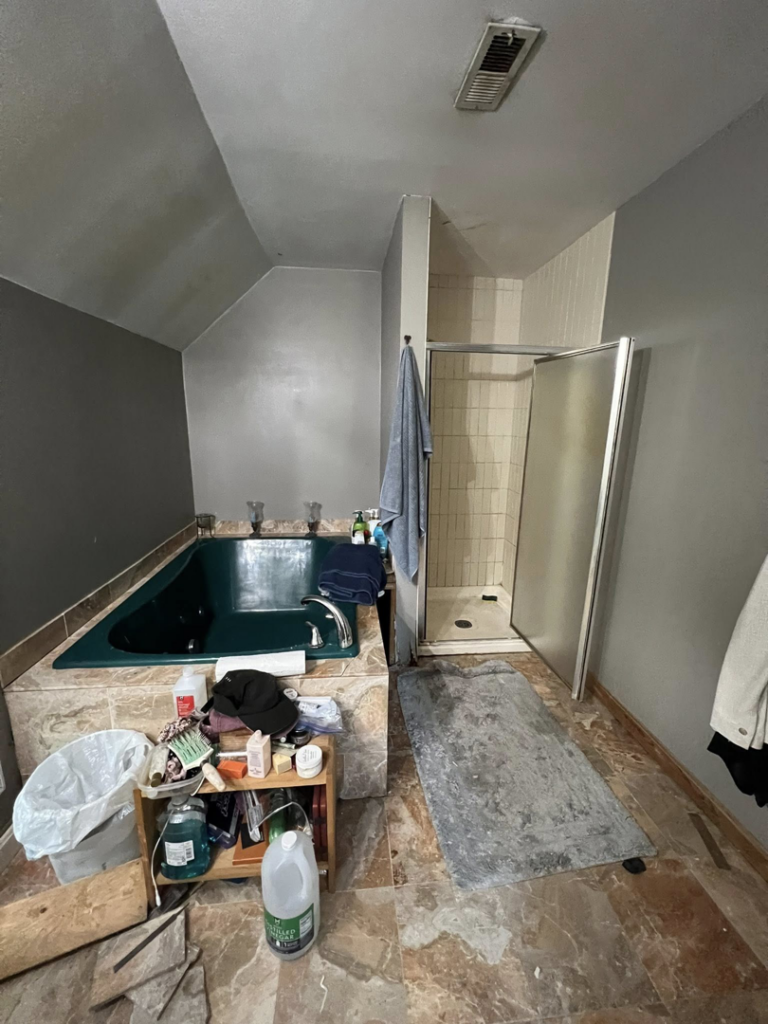 An old and cluttered bathroom with a green tub and small shower, showing a 'before' view for renovation services by Great Home Construction LLC in Annapolis, MD.