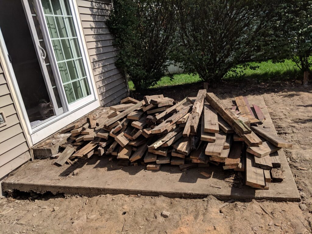 A pile of old wooden decking debris on a concrete patio next to a house, ready for removal by 1-800-Declutter in Cincinnati, OH.
