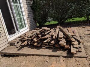 A pile of old wooden decking debris on a concrete patio next to a house, ready for removal by 1-800-Declutter in Cincinnati, OH.