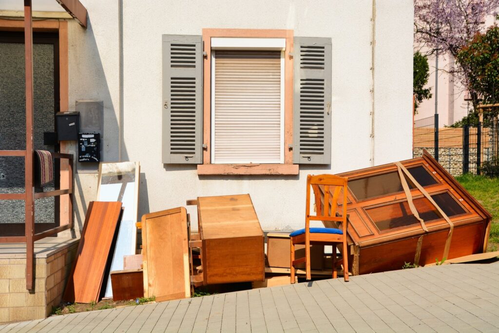 A pile of old wooden furniture, including cabinets and a chair, placed outside a house for removal by Junk Movers in Salt Lake City, UT.