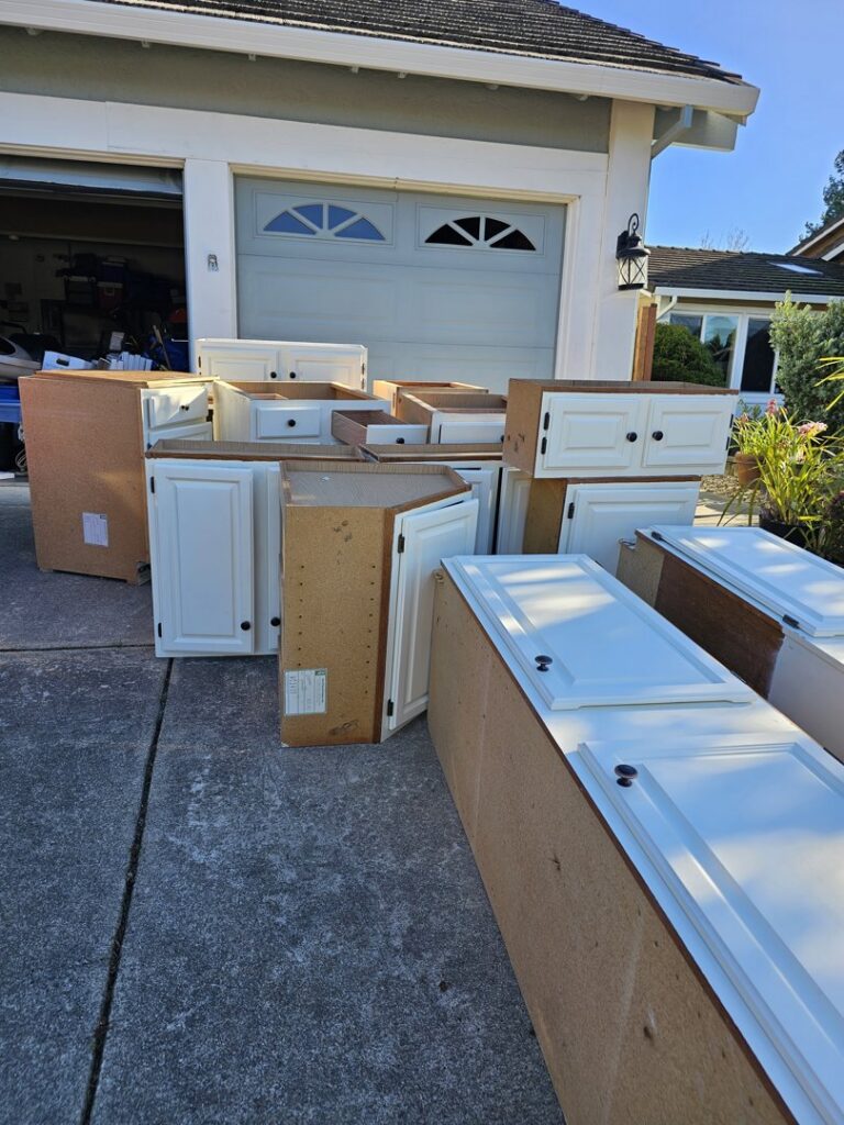 A pile of old kitchen cabinets and other debris outside a garage, ready for Nixxit Junk Removal in Castro Valley, CA.