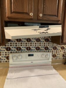 An old, damaged range hood being removed or replaced above a kitchen stove, a service provided by Folmar's Handyman & Remodeling in Lincoln, NE.