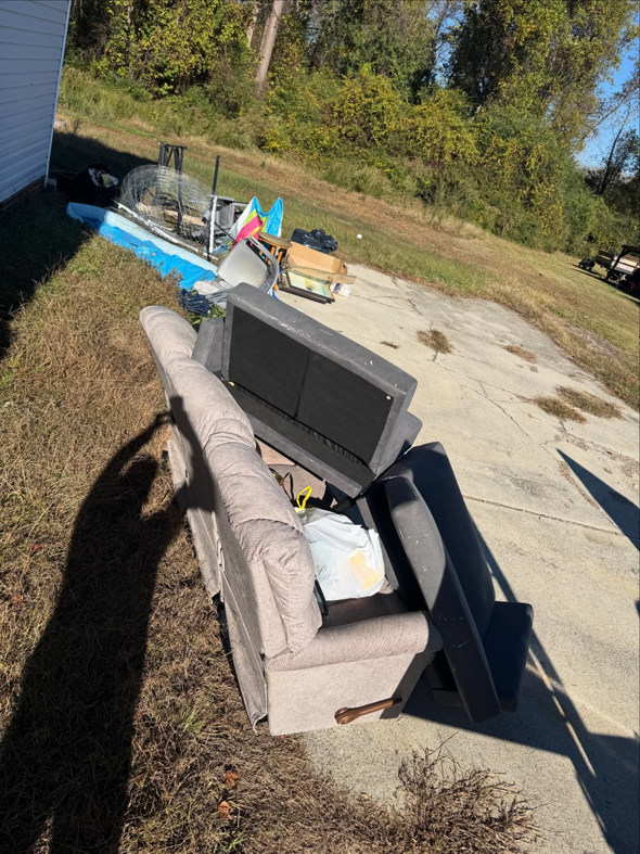 An old recliner and various household junk items piled on a driveway for removal by Junkslingers NC in Cary, NC.