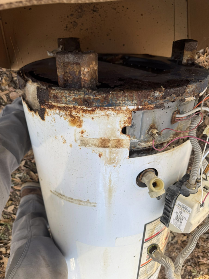 An old, rusty, and damaged water heater being removed, a service provided by High Tide Home Remodeling in Charleston, SC.