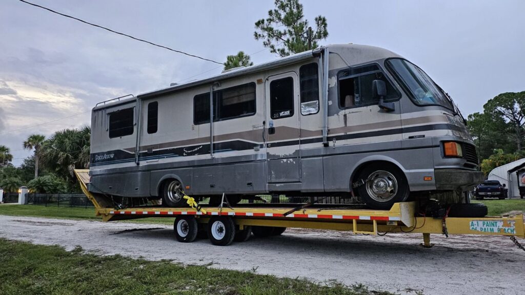 An old, worn-out RV being hauled away on a flatbed trailer by AAA Rousse Junk Removal Services Inc of Florida in Tampa, FL.