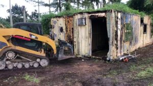 Gator Junk Removal using a skid steer to remove a dilapidated shipping container from a property in Miami, FL.