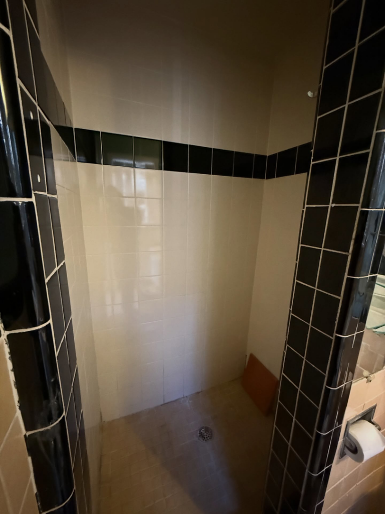 An old shower with beige and black tiles, showing a 'before' view of a renovation project by Waking Up Construction in Oklahoma City, OK