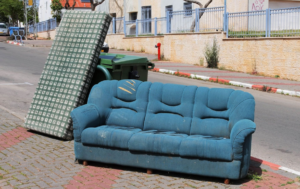 An old blue sofa and mattress discarded on a sidewalk, awaiting furniture removal by 1-888-PIK-IT-UP in Cary, NC.