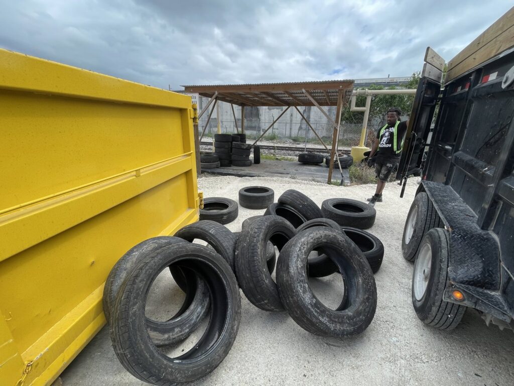 A pile of old tires ready for removal by Gator Junk Removal, with a dumpster and trailer nearby in Miami, FL.