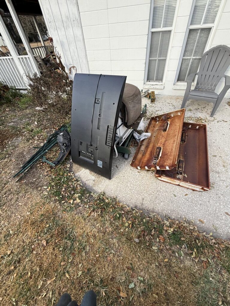 A pile of old TV, wooden panels, and other debris outside a house, ready for junk removal by Lightning Bay Junk Removal in Tampa, FL.