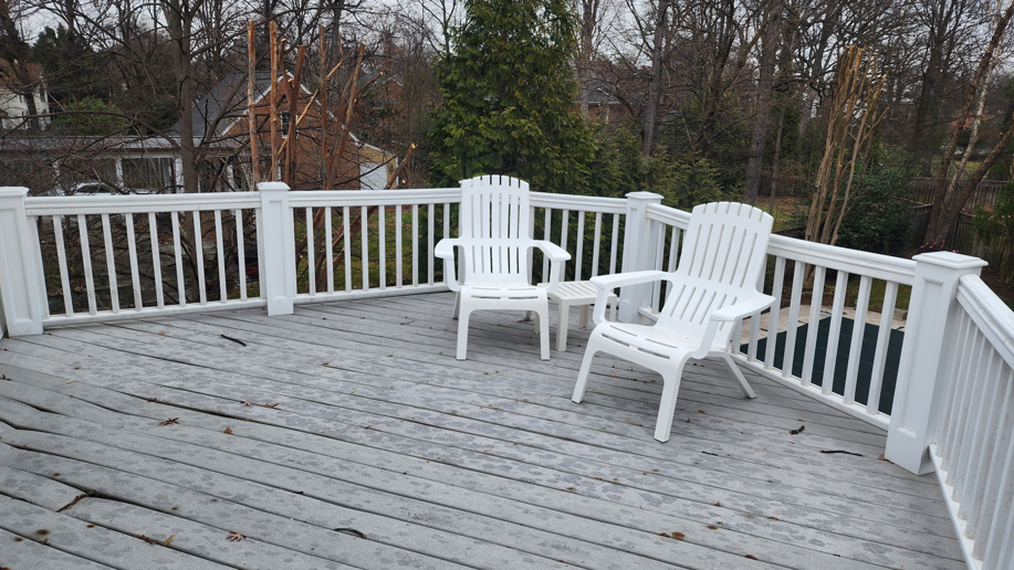 An old, weathered wooden deck with white railings and chairs, in need of refinishing or repair by Sundecks, Inc. in Manassas, VA.