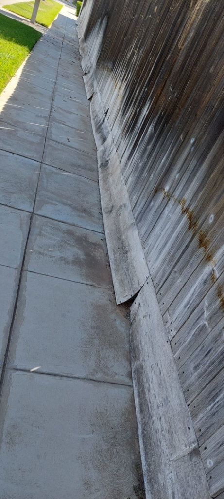 An old, weathered wooden fence needing repair alongside a concrete path, a service offered by Montano's Handyman in Fresno, CA