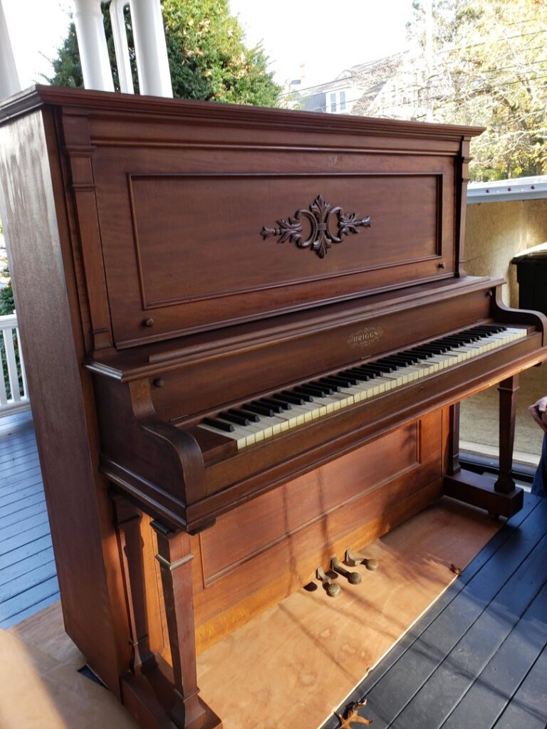 An old wooden upright piano ready for removal from a porch by Green Clover in Quincy, MA.