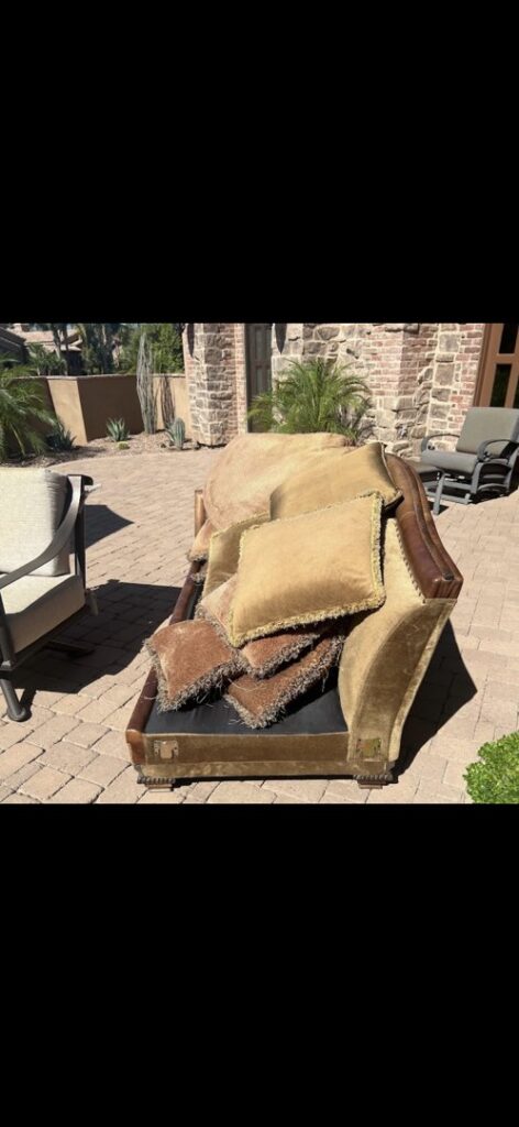 An old, worn-out couch with decorative pillows placed on a patio, ready for removal by The Junkporter Junk Removal in Las Vegas, NV.
