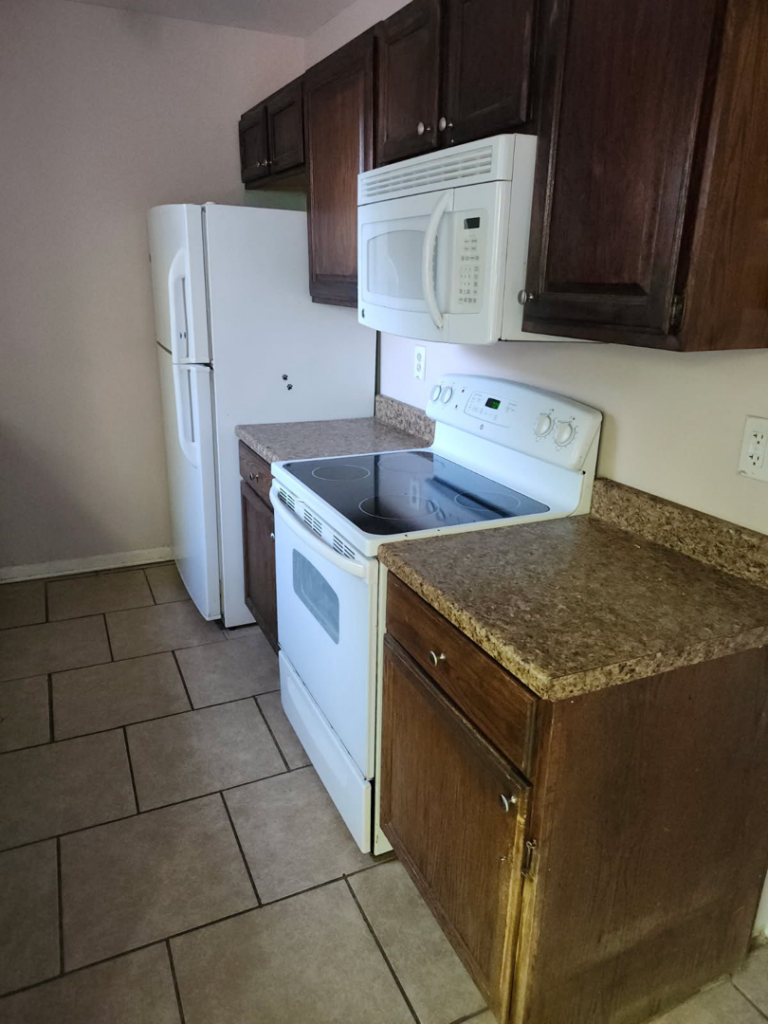 An older kitchen space with dark cabinets and white appliances, suitable for handyman updates by Wareham Home Improvements in Frederick, MD.