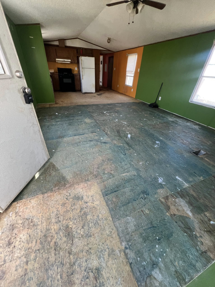 An open-concept room with the subfloor exposed and a kitchen area in the background, showing renovation work by Cosa Cleanouts & Junk Removal in Topeka, KS.