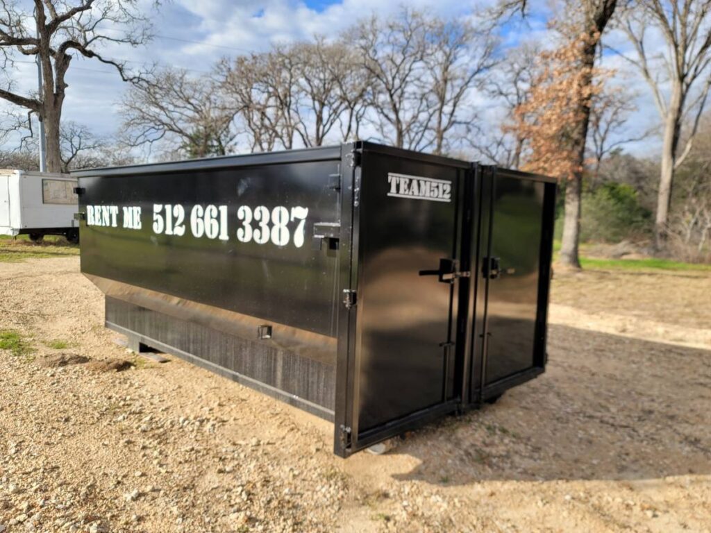 An open black roll-off dumpster from Team512 with 'RENT ME' signage, ready for waste disposal in Austin, TX