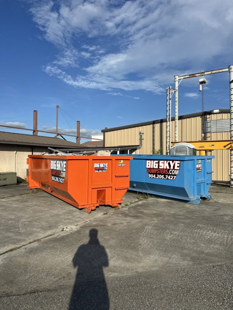 An orange and a blue dumpster from Big Skye Dumpsters placed at a commercial site in Jacksonville, FL.