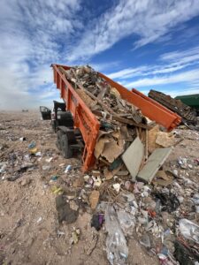 An orange dump trailer from Easy Load Disposal El Paso unloading a large pile of mixed junk and debris in El Paso, TX.