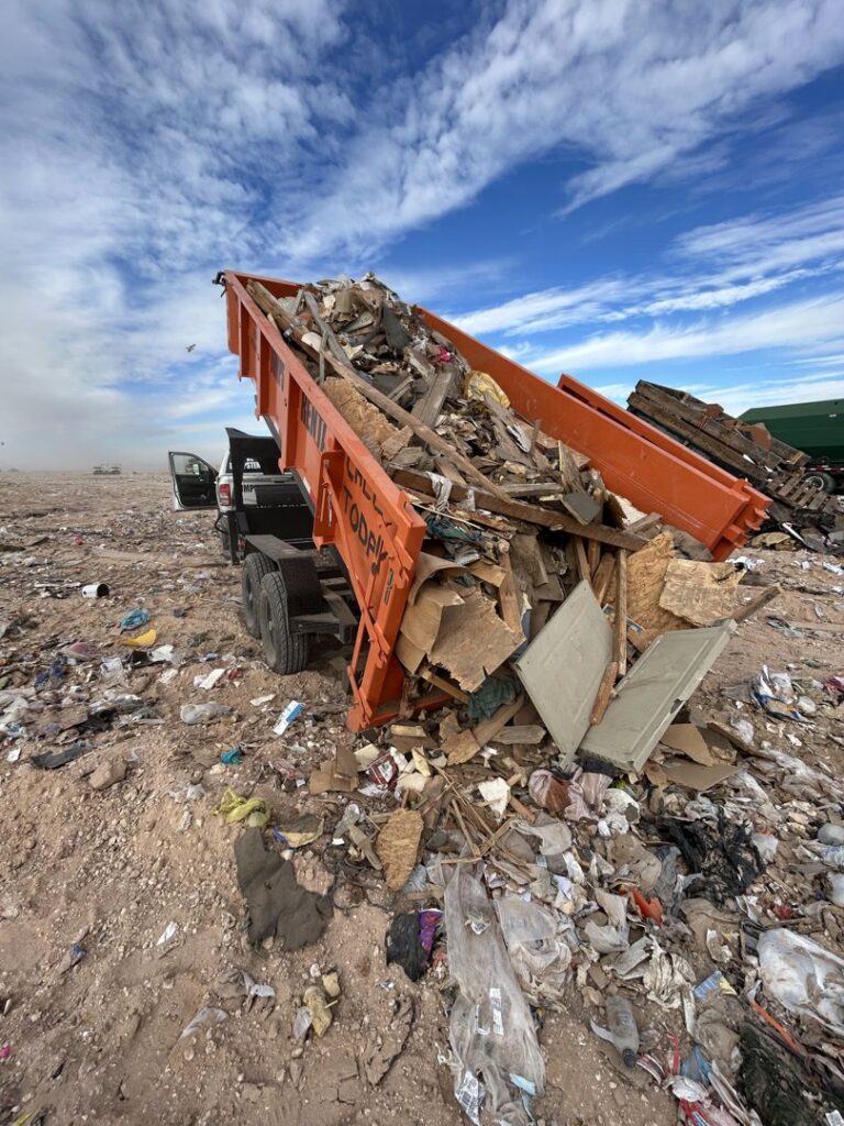 An orange dump trailer from Easy Load Disposal El Paso unloading a large pile of mixed junk and debris in El Paso, TX.