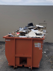 An orange roll-off dumpster filled with construction debris and junk, provided by Century Waste Management in Sterling Heights, MI.
