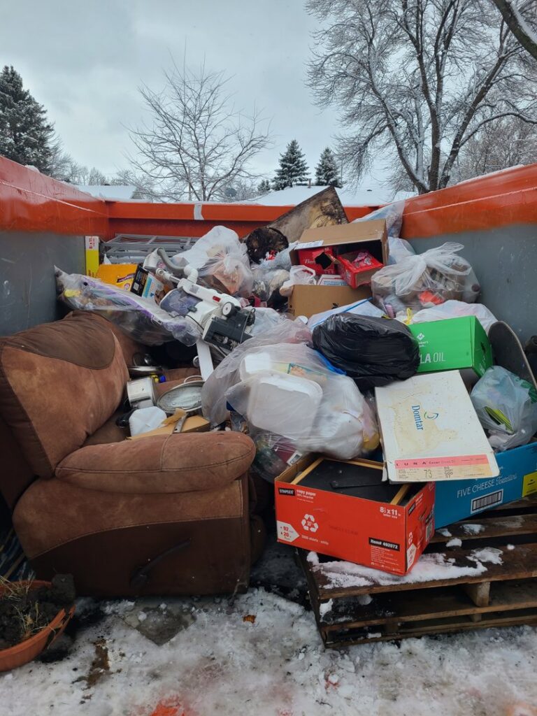 An orange roll-off dumpster filled with various junk items for removal, a service provided by Red River Removal in West Fargo, ND.