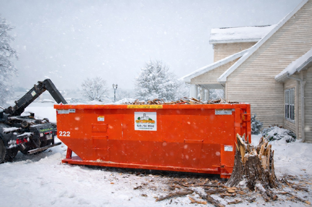 An orange roll-off dumpster from City Disposal Services Inc. filled with debris next to a house in Appleton, WI.