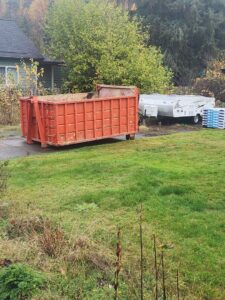 An orange roll-off dumpster placed in a residential yard by ADE Hauling in Tacoma, WA
