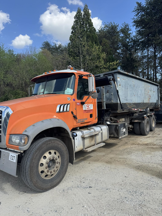 An orange Mack truck with a roll-off dumpster attached, used by Stryker Environmental Inc for junk removal in Bethel Dr., GA.