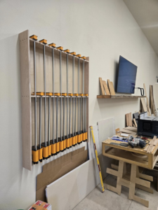 An organized woodworking workshop featuring a wall-mounted clamp rack and tools, used by Kingsbury Builders LLC in Janesville, WI