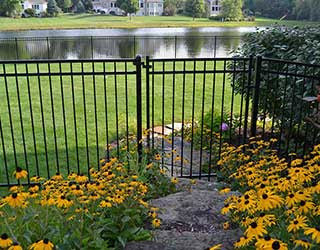 An ornamental black metal fence with a gate installed near a garden by R & C Fence in Fort Wayne, IN.