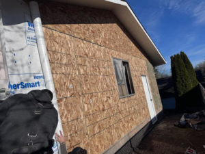 A worker installing OSB sheathing and house wrap on a residential exterior by CJ Hansen Construction in North Bend, OR.