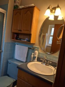 An outdated blue tiled bathroom with a wooden vanity, showing a before shot of a remodel by Better Than Your Last Handyman in St. Charles, MO.