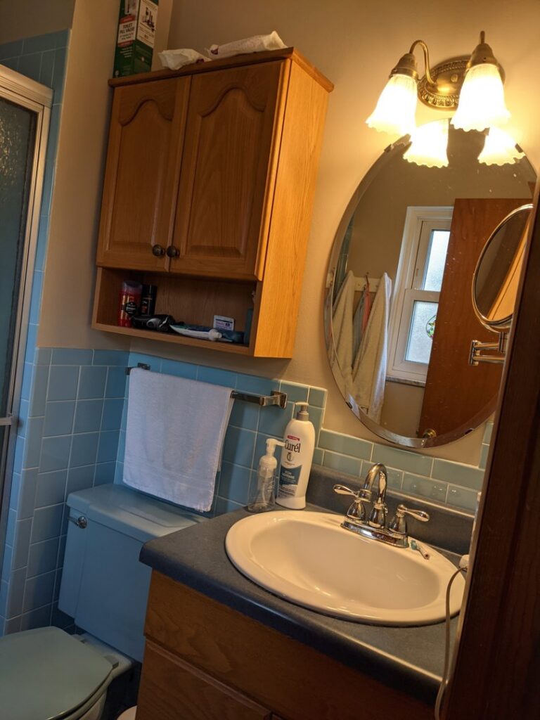An outdated blue tiled bathroom with a wooden vanity, showing a before shot of a remodel by Better Than Your Last Handyman in St. Charles, MO.