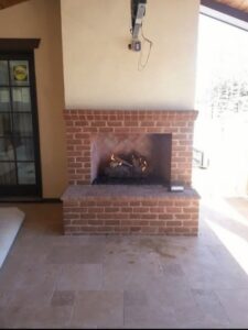 An outdoor brick fireplace with a fire burning, expertly installed by Infinite Fire Features in Colorado Springs, CO.