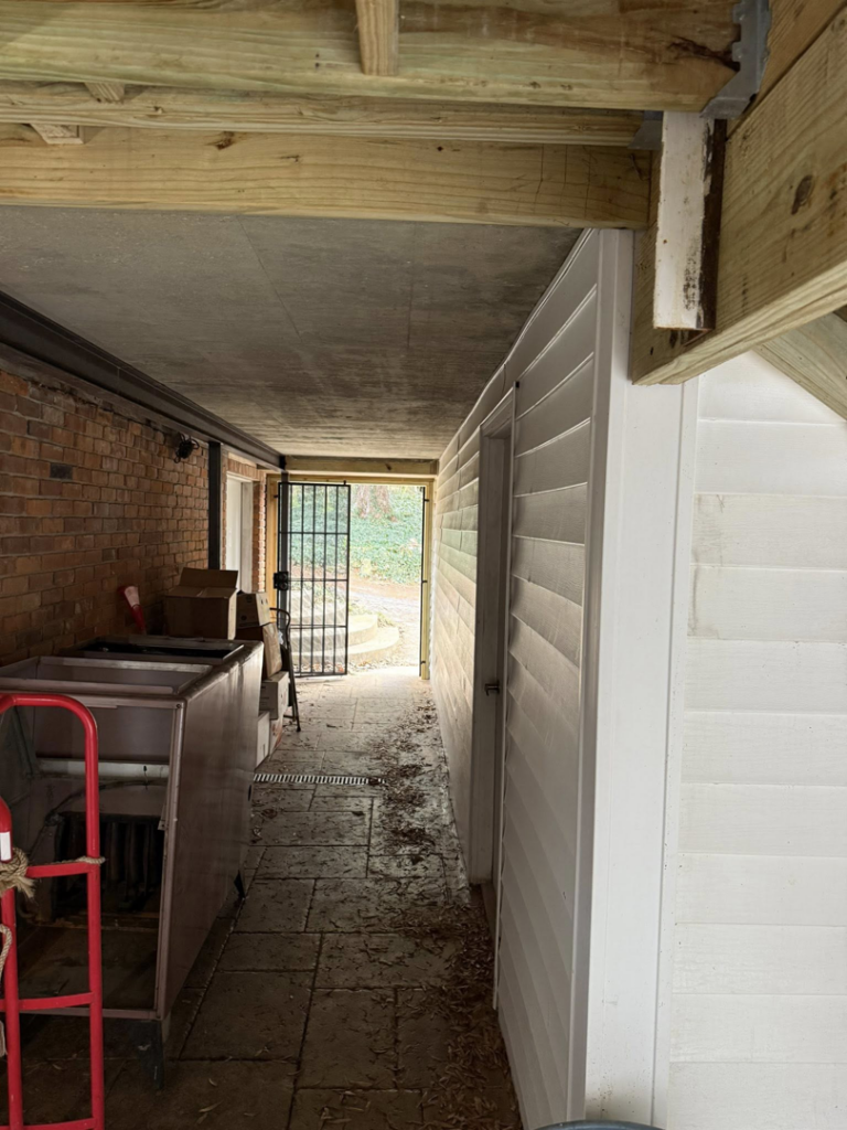 A newly constructed outdoor covered walkway with fresh white siding and wooden support beams by Rogers Remodeling in Bloomington, IN.