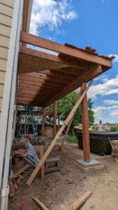 An outdoor deck or pergola structure under construction, showing wooden beams and supports by The Foundation Guys in Lakewood, CO