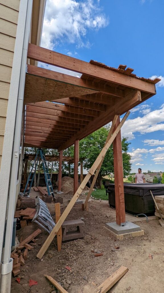 An outdoor deck or pergola structure under construction, showing wooden beams and supports by The Foundation Guys in Lakewood, CO