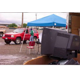 An outdoor e-waste collection event with old televisions and a person under a tent, managed by E-Waste Recovery Systems in Sacramento, CA.