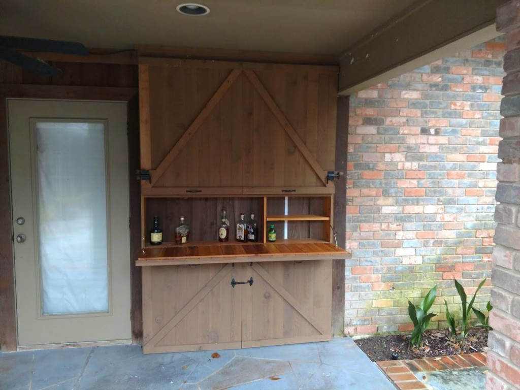 A custom outdoor entertainment and bar cabinet, showing the bar section open, completed by Rex Austin's Remodeling in Ball, LA.