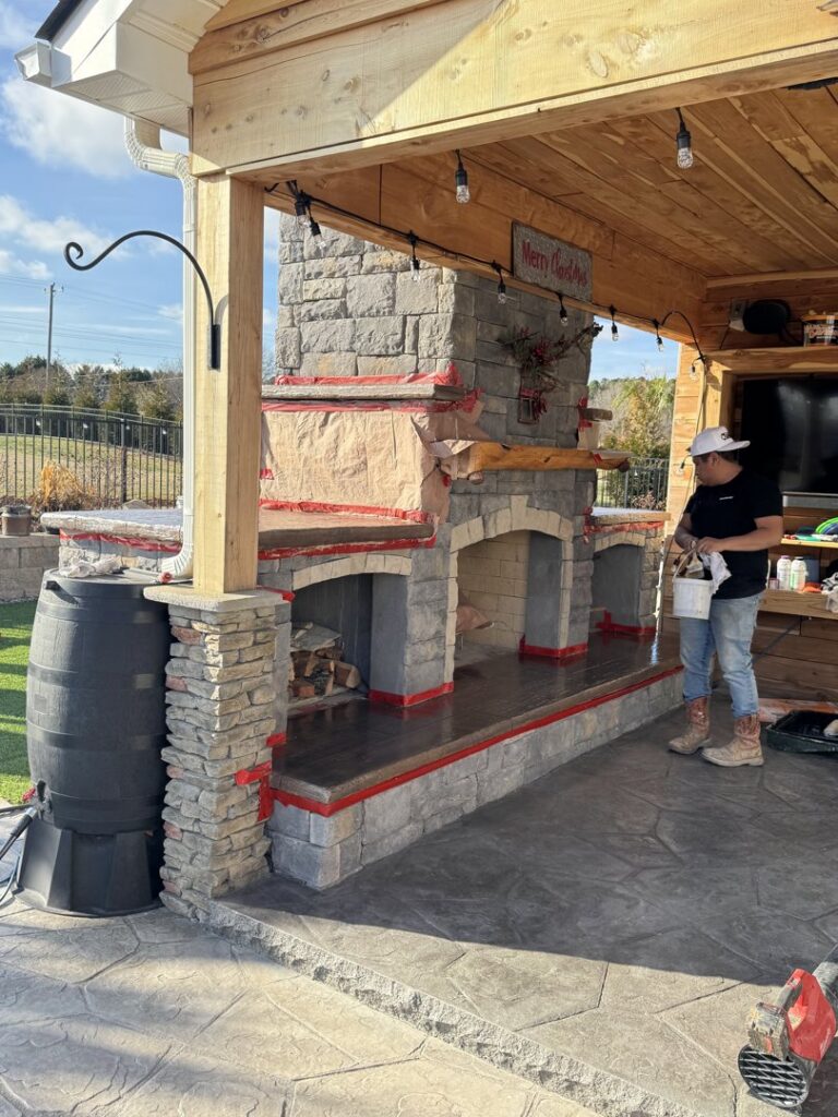 A worker standing by a large outdoor fireplace and kitchen structure under construction by Rodriguez Concrete Creations in Rock Hill, SC.