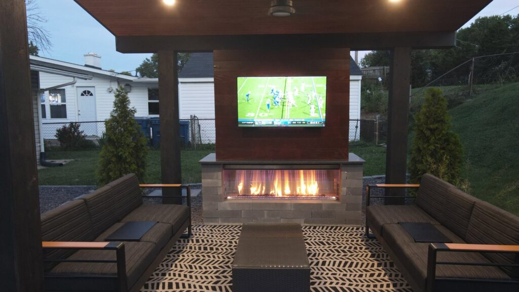 An outdoor fireplace with a mounted TV under a covered patio by Rescue Landscaping and Outdoor Living in St. Louis, MO.
