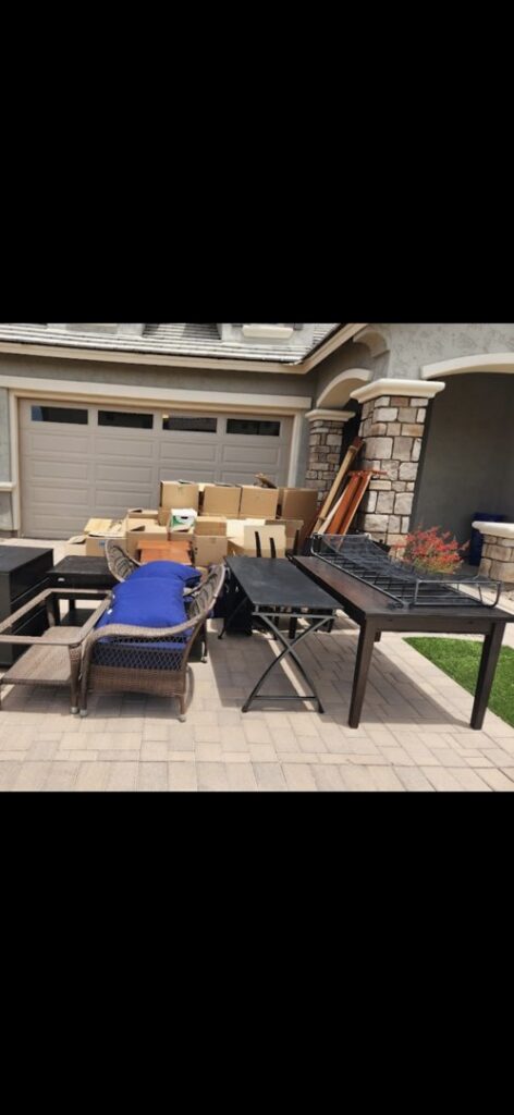 Outdoor furniture, tables, chairs, and cardboard boxes piled outside a garage for removal by The Junkporter Junk Removal in Las Vegas, NV.