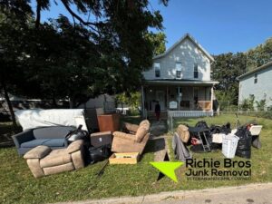 A large pile of old furniture and trash bags outside a house, awaiting pickup by Richie Bros Junk Removal in Urbandale, IA.